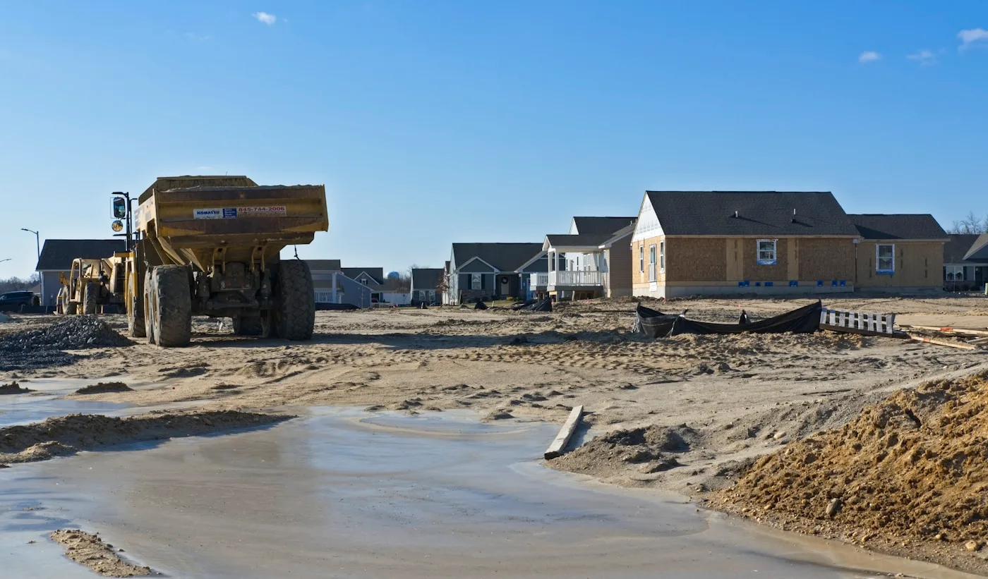 Construction site with a dump truck and houses in the background