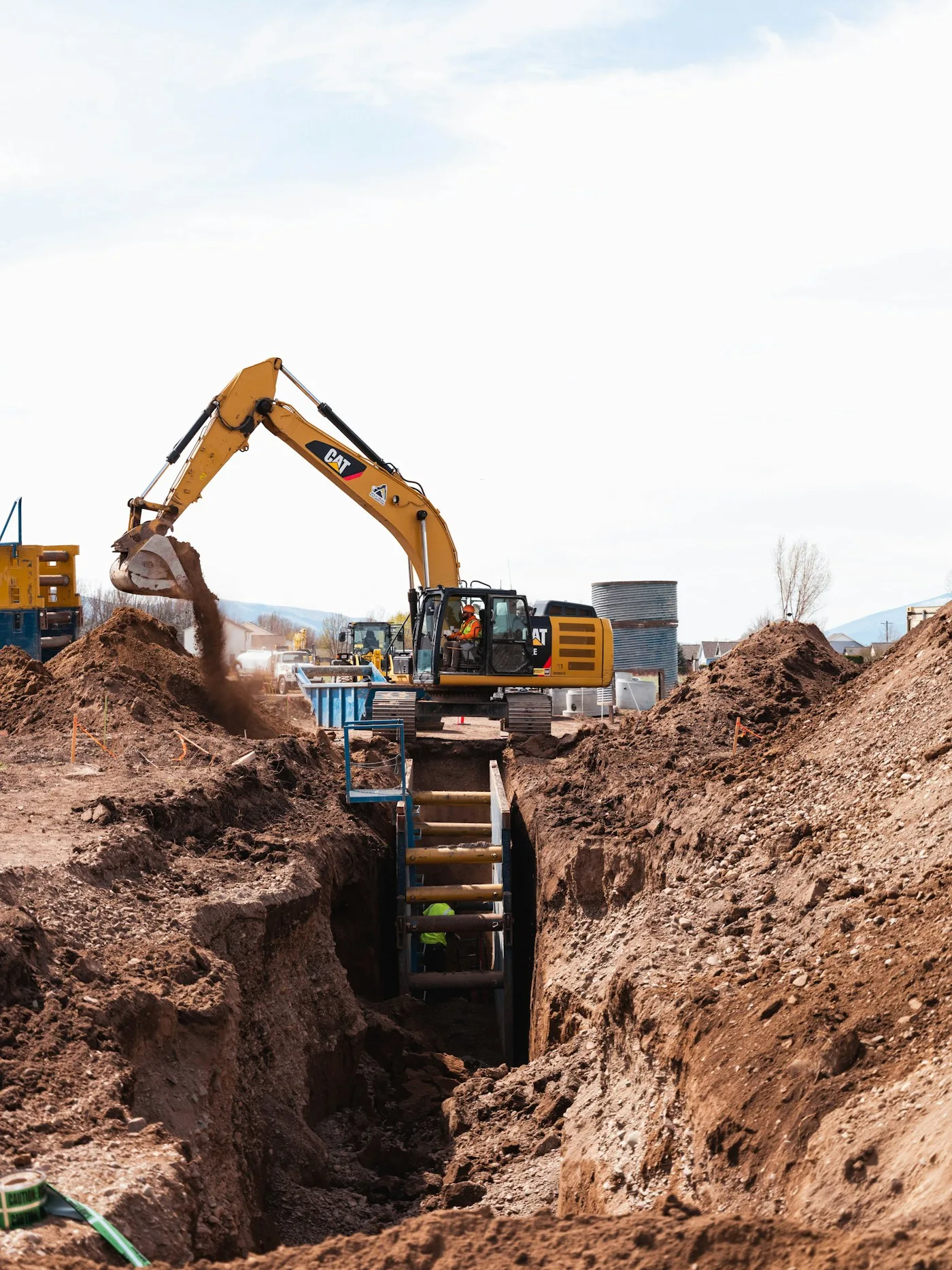 Excavator digging a trench with a worker in hi-vis gear on an active jobsite