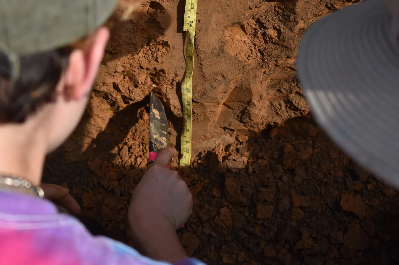 People examining soil layers with a measuring tape in a soil pit